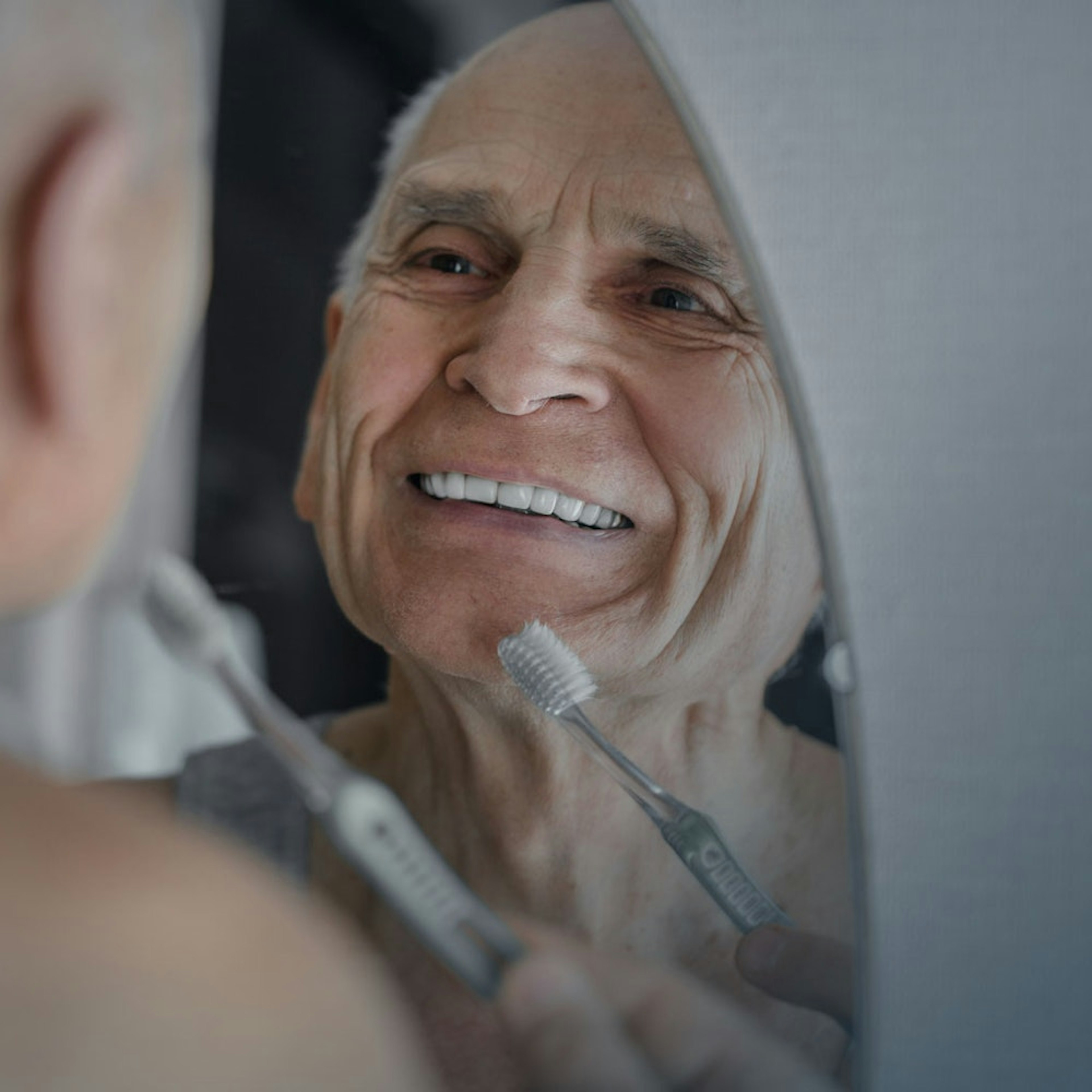 Older man looking in the mirror while brushing his teeth