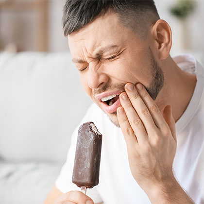 man suffering from gum disease eating ice cream and holding jaw in pain
