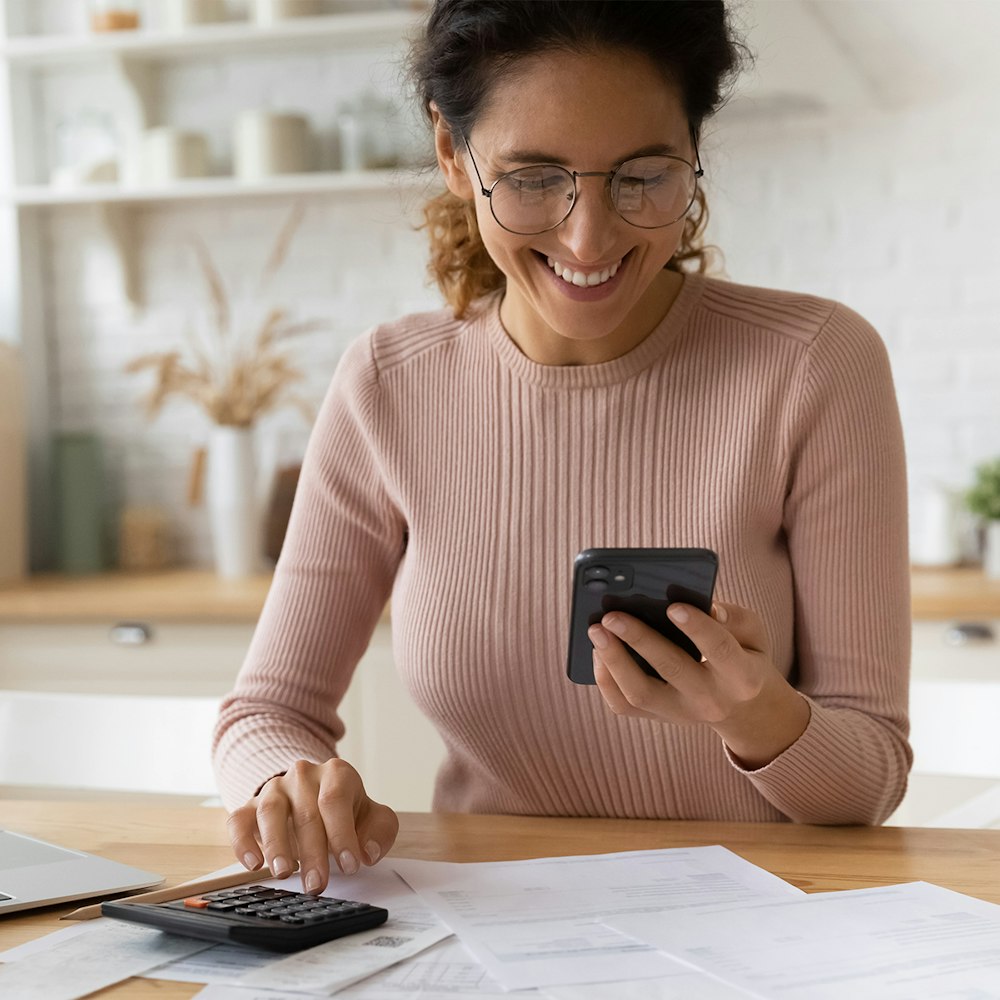 Smiling woman looking at phone and calculator