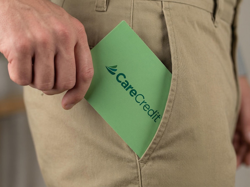 Close-up of a person placing a green CareCredit brochure into their pants pocket.