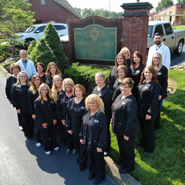 Team of Newport Family Dental Care staff standing outside the office sign, with Dr. David Sutton and Dr. Joseph Sutton wearing white lab coats