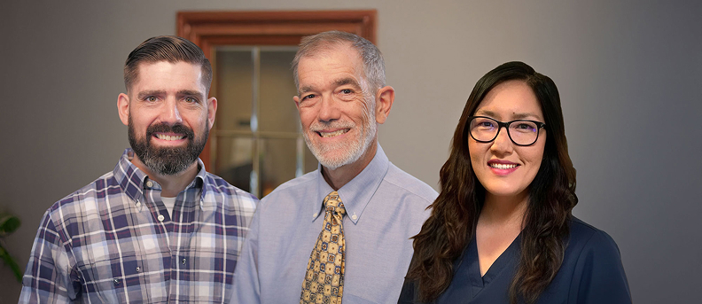 Dr. Joseph Sutton, Dr. David Sutton, and Dr. Hannah Yi standing together and smiling at Newport Family Dental Care