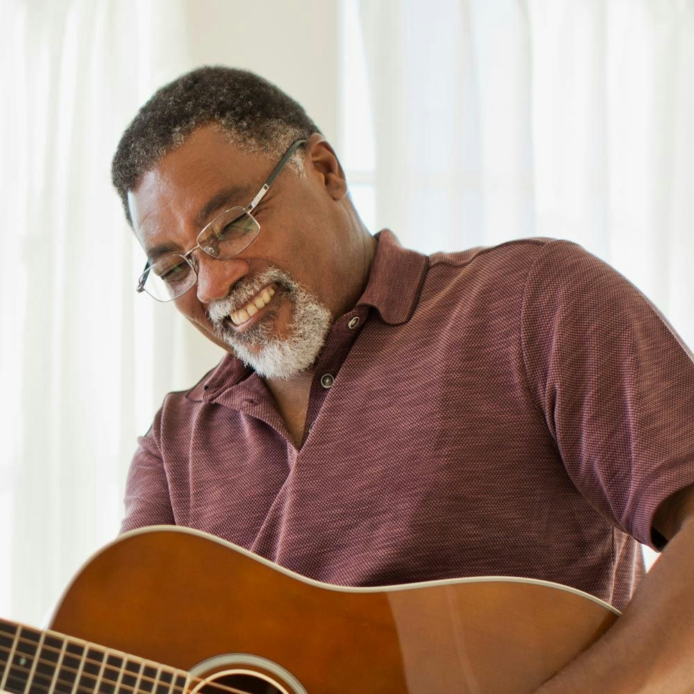 Older man smiling while playing guitar