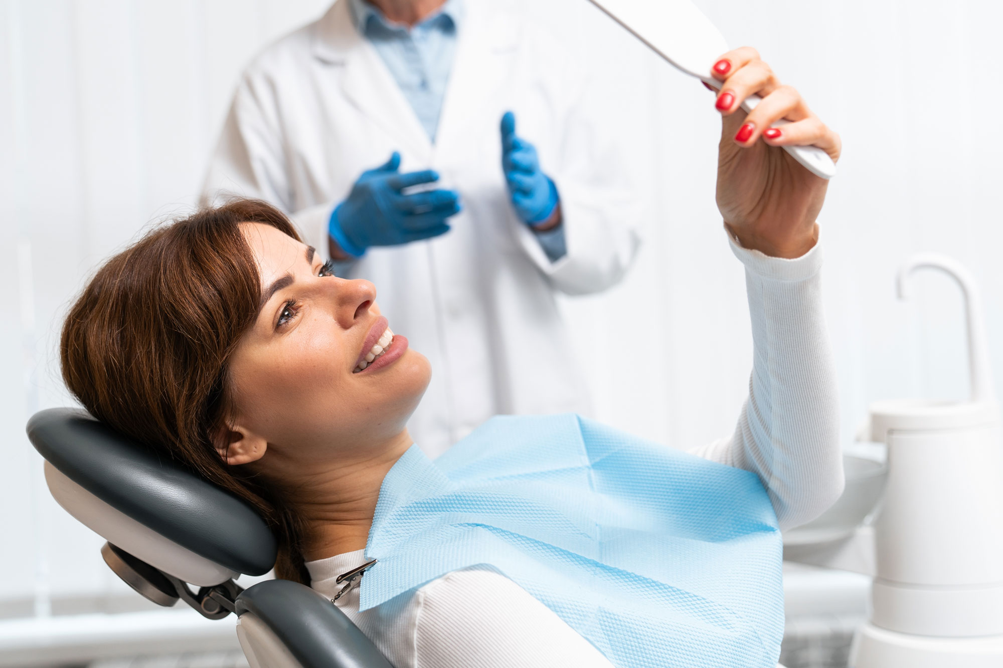Cosmetic dentistry patient smiling in a hand mirror at the dentist