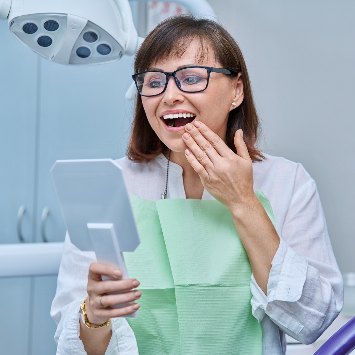 woman looking at teeth in mirror after placement of implant-supported restoration