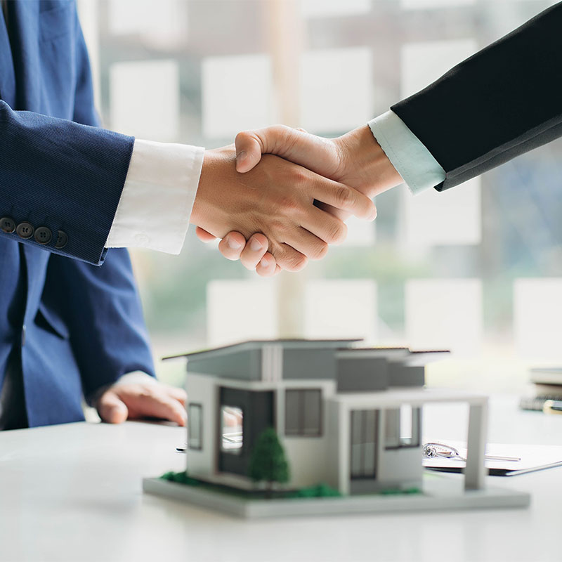 shaking hands over a model of a home