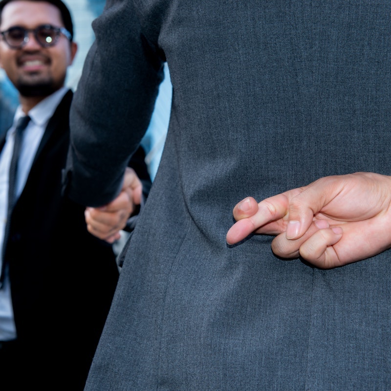 Business man crossing his fingers behind his back while shaking hands