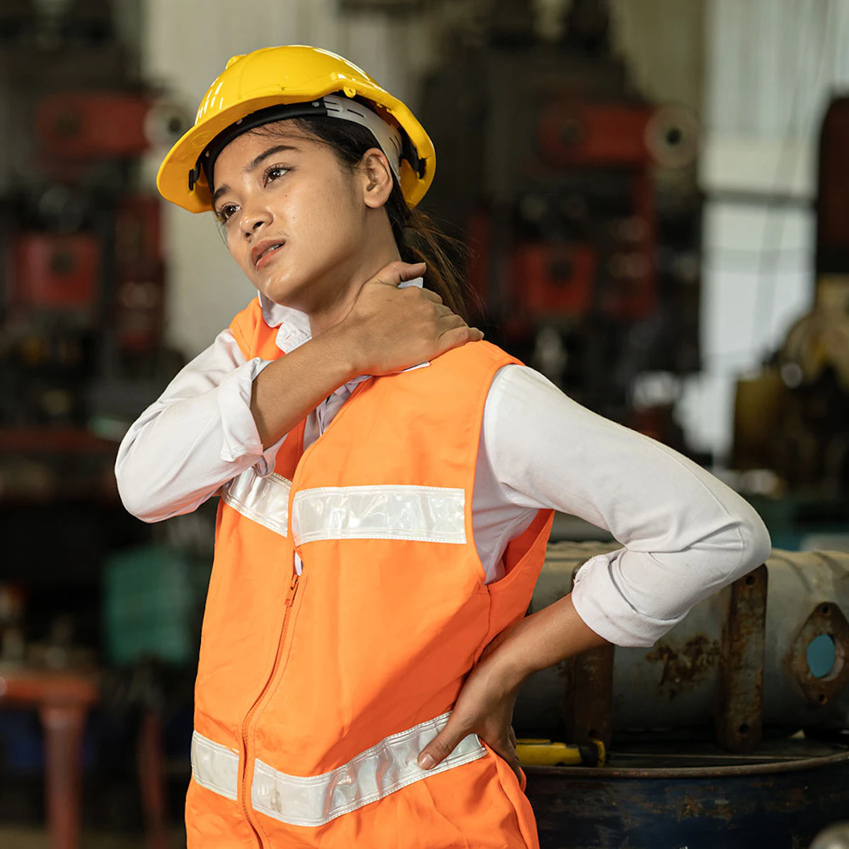 Construction worker in a hard hat and safety vest holding her shoulder in pain on a job site