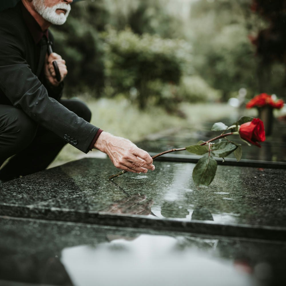 Mature man putting rose on tombstone