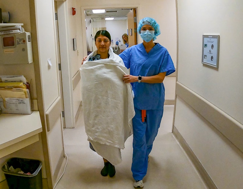 Patient walking down the hallway in surgical garb with nurse