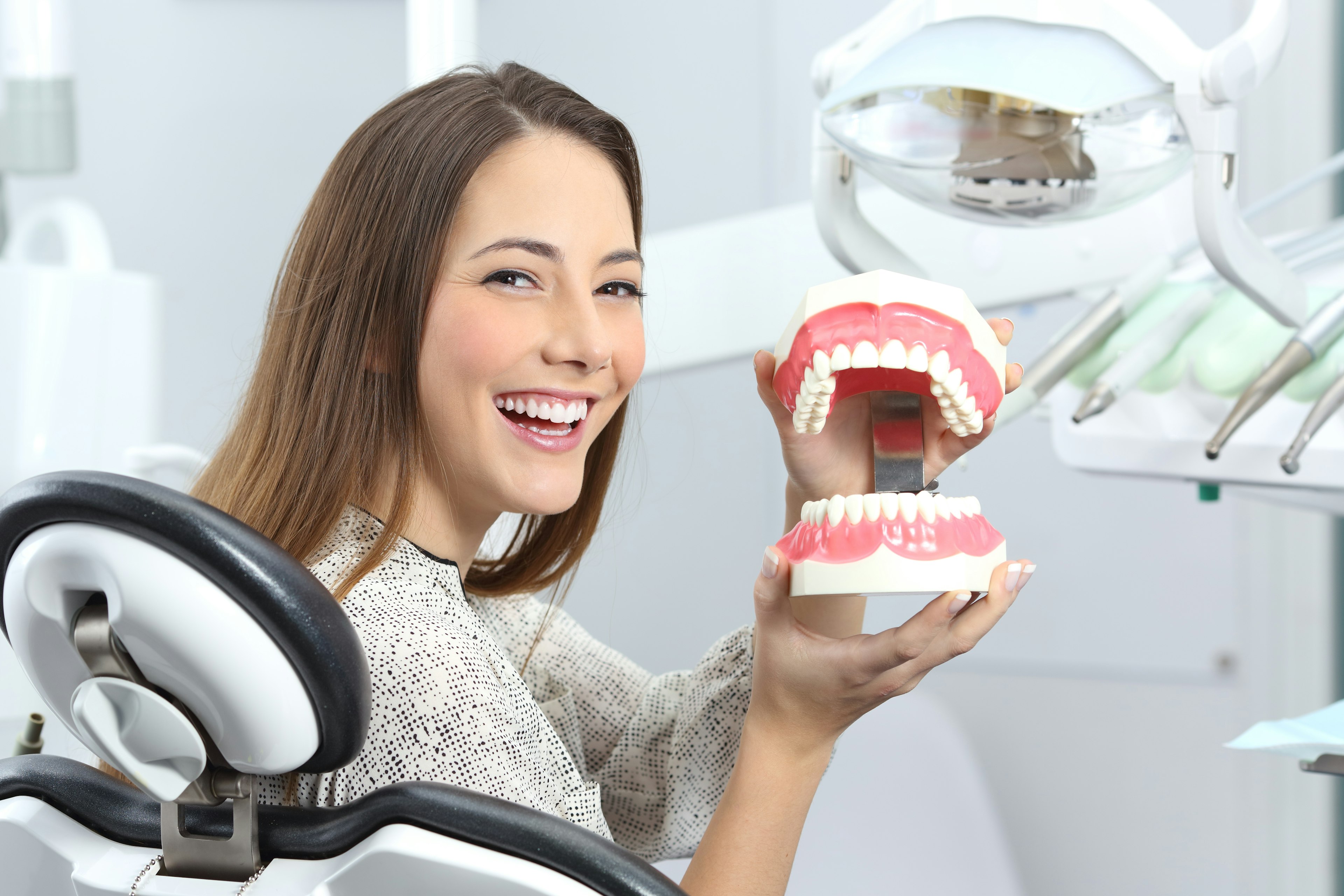 Smiling woman in dentist's office holding large model of teeth
