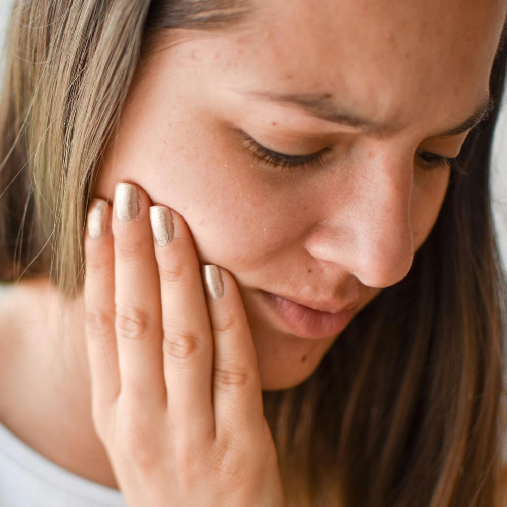 Woman placing one hand on her jaw in pain