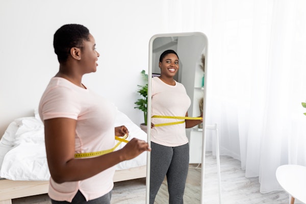 Happy woman looking in the mirror and measuring her chest