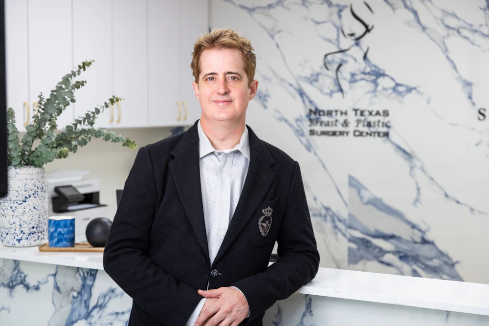 Dr. Bruce Hermann in a blazer at the front desk of North Texas Breast & Plastic Surgery Center