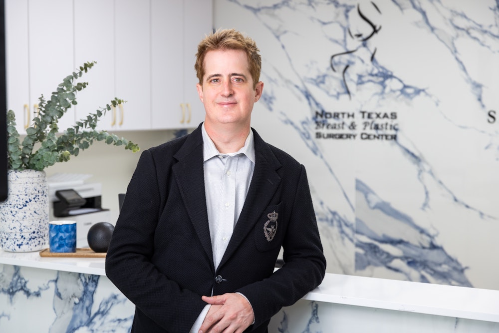 Dr. Bruce Hermann in a blazer at the front desk of North Texas Breast & Plastic Surgery Center