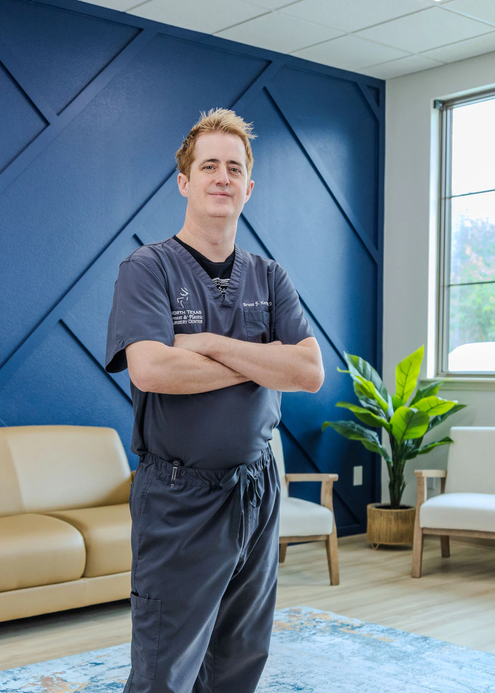 Dr. Bruce Hermann smiling in scrubs at North Texas Breast & Plastic Surgery Center