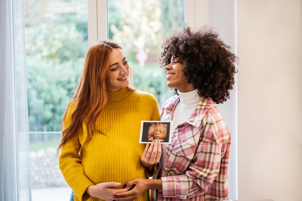 Pregnant woman and female partner smiling while holding a sonogram photo