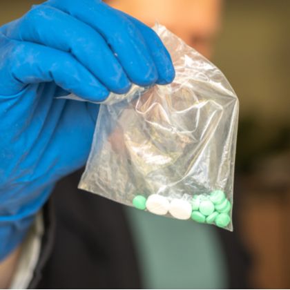Man wearing blue gloves holding up small plastic bag of pills