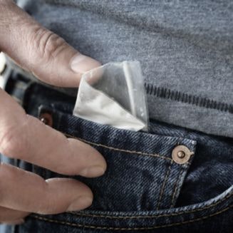 Man putting small plastic bag of powder into jean pocket