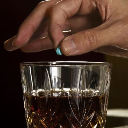 Man dropping pill in whiskey