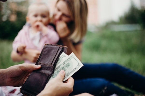 Person taking money from wallet, with baby and woman in the background