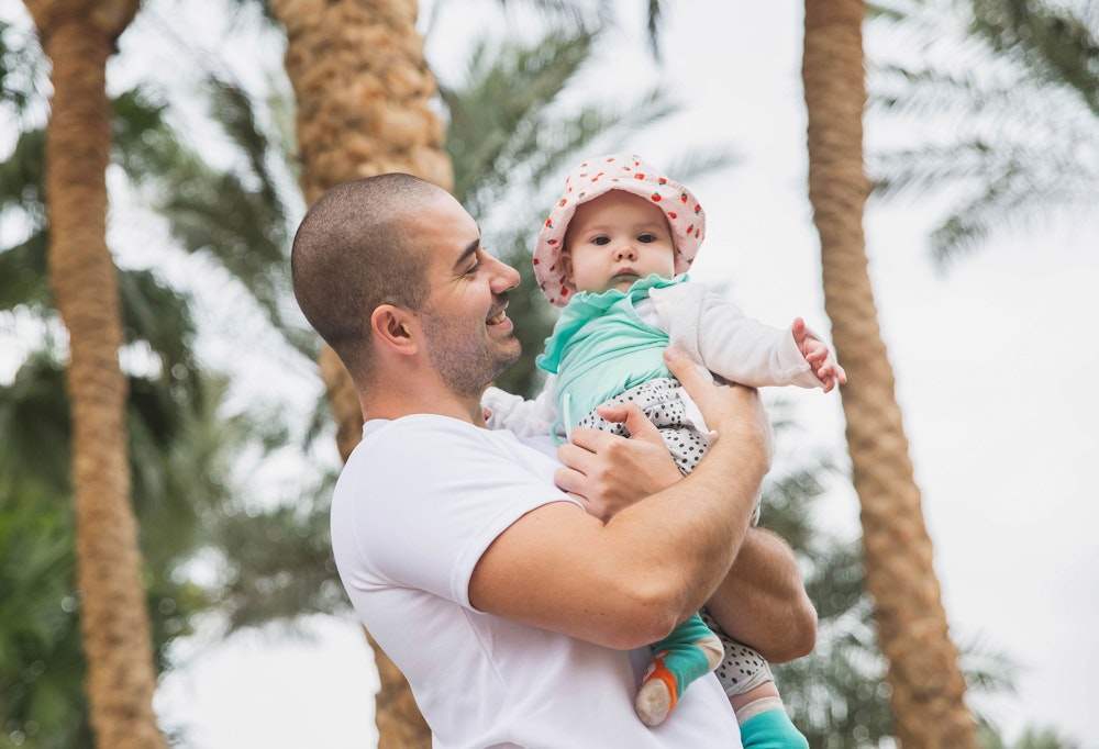 Father holding baby with palm trees in the background