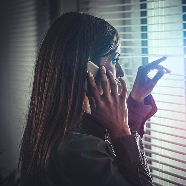 Woman talking on the phone and looking through window blinds