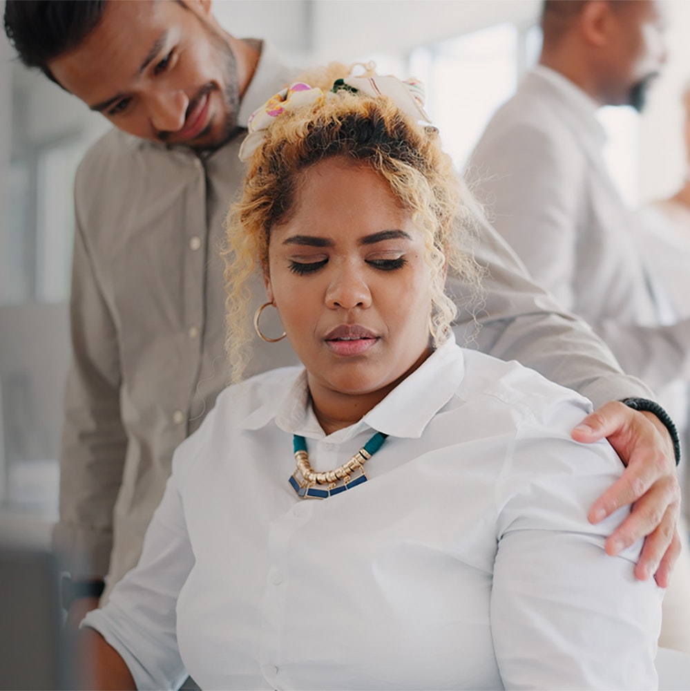 Girl looking uncomfortable at her desk while a man's hand is on her shoulder