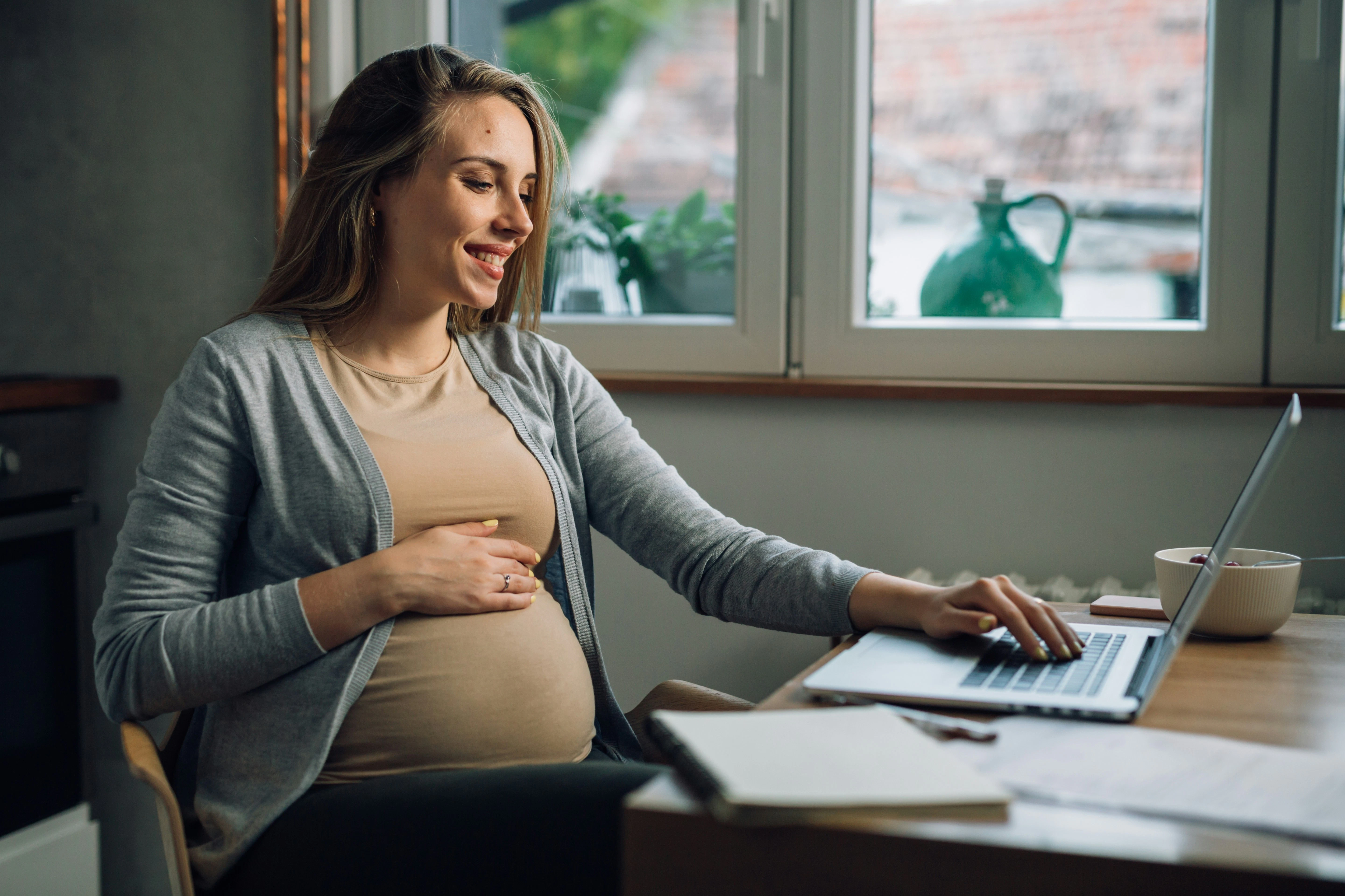 Pregnant woman holding stomach on her laptop