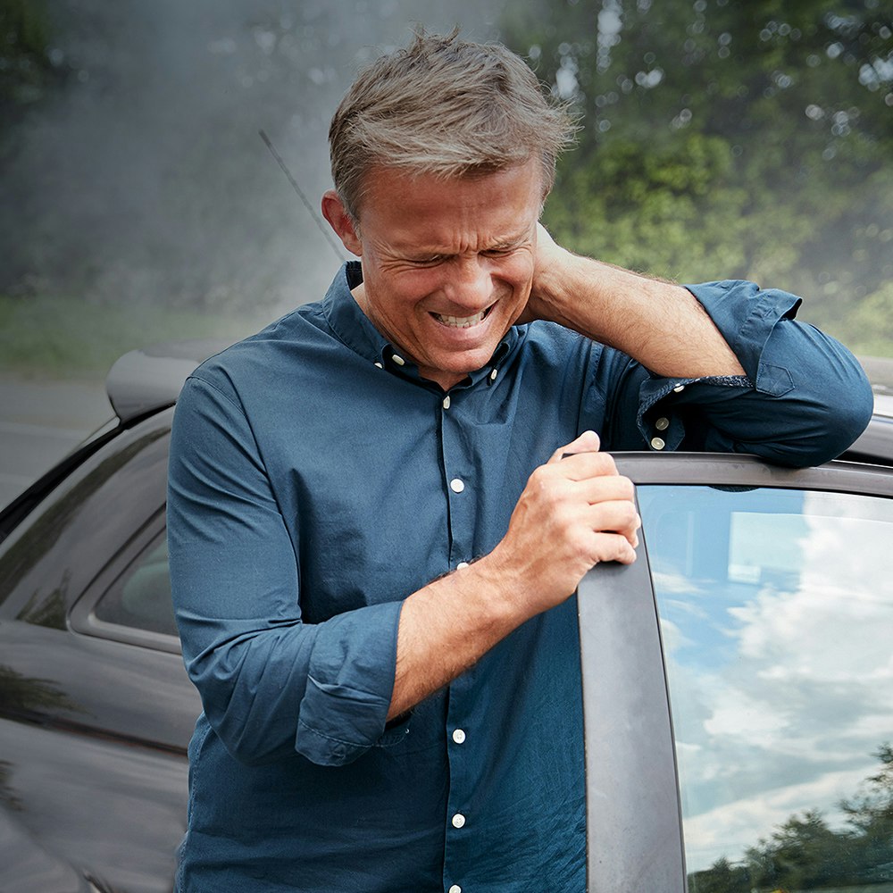 Woman sitting on ground against car wheel, hands over face