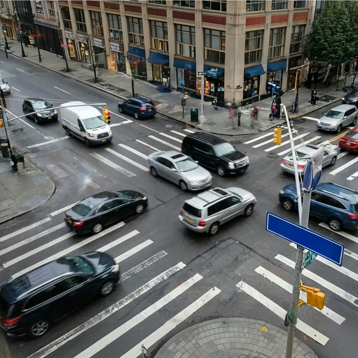 Busy urban intersection with cars in motion and pedestrians on the sidewalk near a crosswalk.