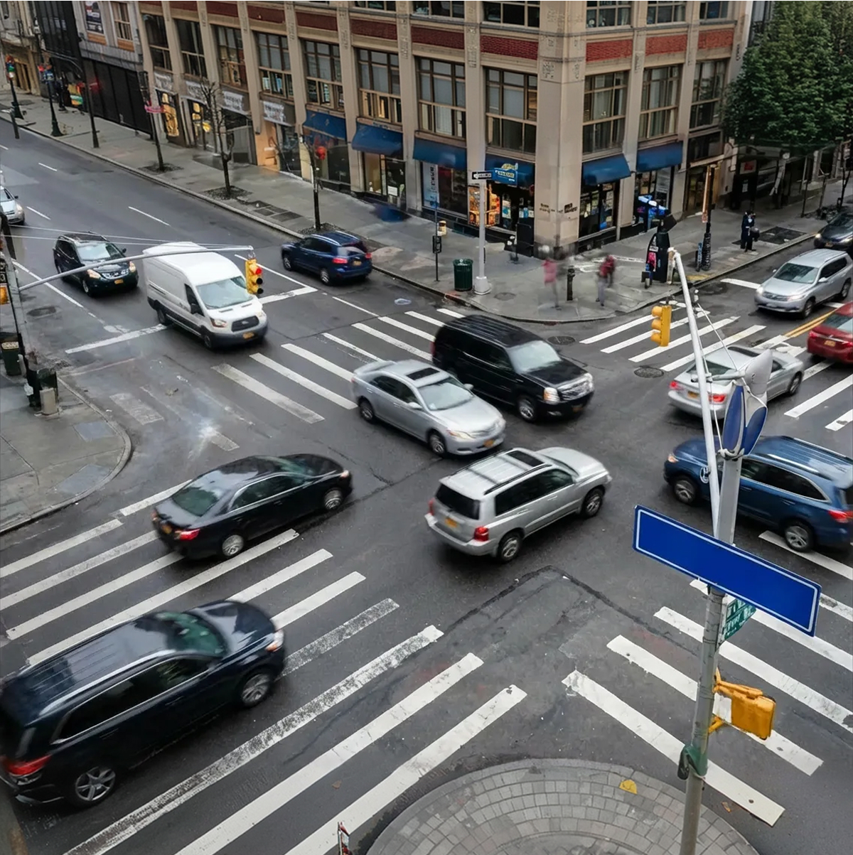 Busy urban intersection with cars in motion and pedestrians on the sidewalk near a crosswalk.