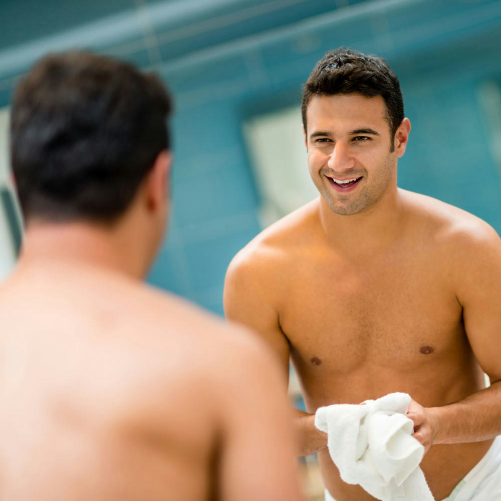 Shirtless man looking in the mirror confidently