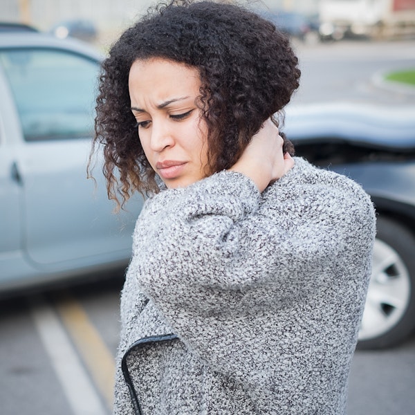 Woman rubbing neck standing outside of wrecked cars