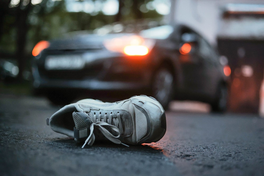 Single sneaker lying in the street in front of a stopped vehicle, suggesting a pedestrian‑vs‑car incident.