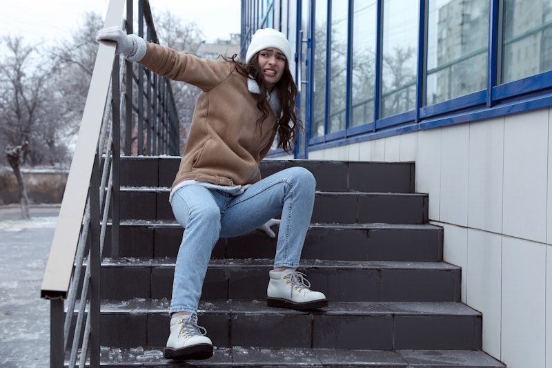 Young woman in winter clothing slipping on icy stairs outside a building