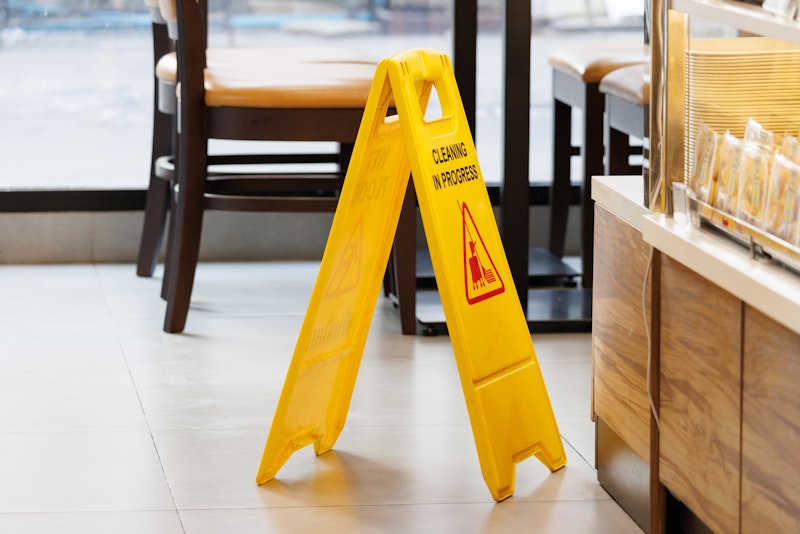 Yellow “Cleaning in Progress” sign on tile floor near café seating