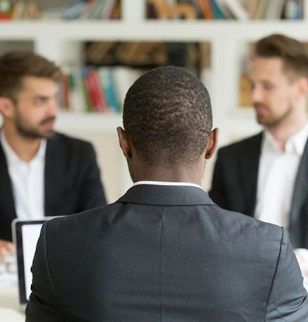 Black businessman sitting in front of two white businessmen
