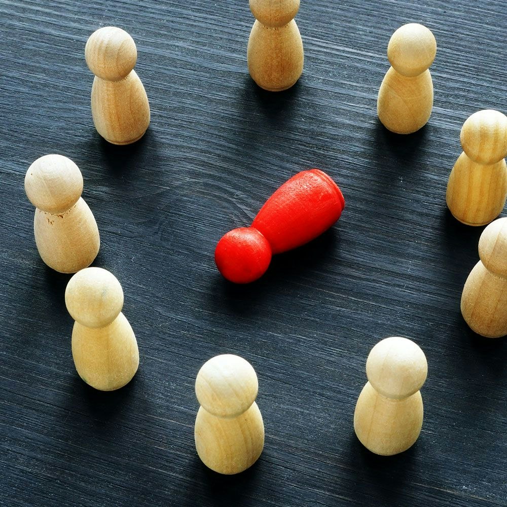 wooden people standing around a red wooden person that has been knocked over
