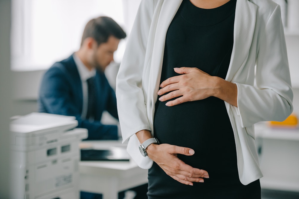 Pregnant woman holding stomach near male coworker