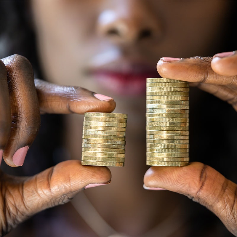 Woman holding two stacks of uneven coins demonstrating the wage gap