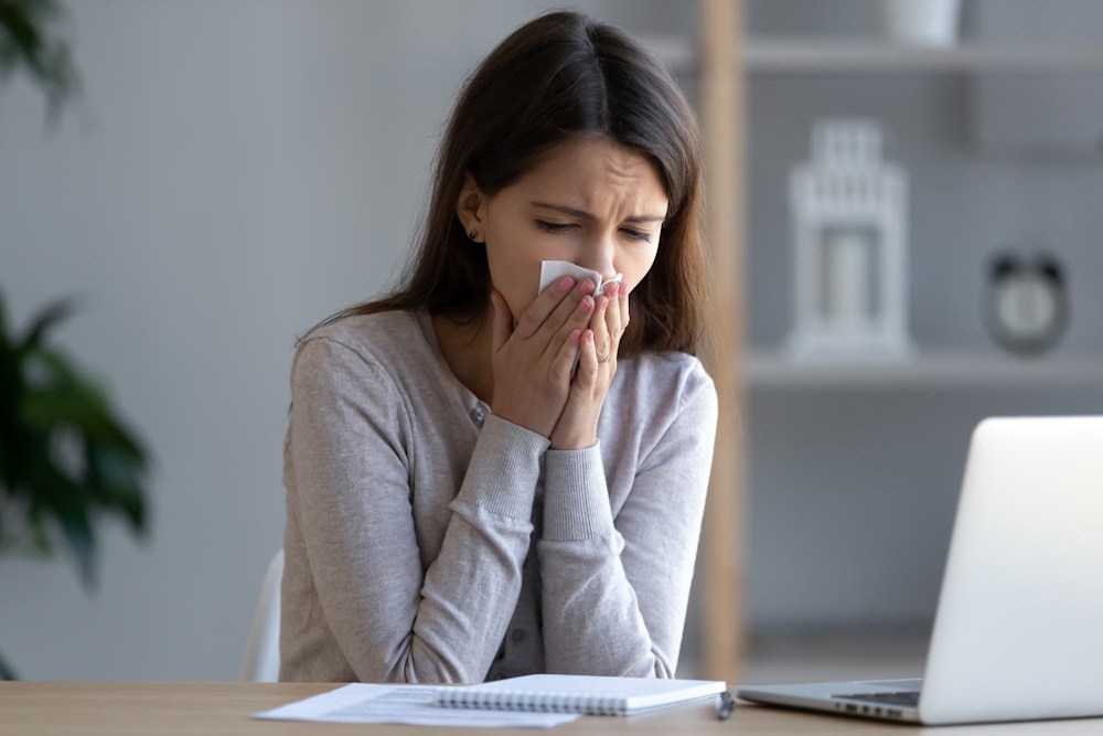 Woman blowing nose at desk