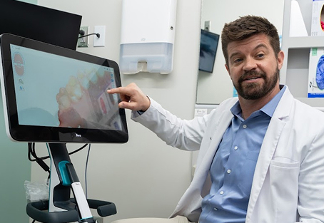 Dr. Burton Gooch pointing to a digital scan of teeth on a touchscreen monitor in a dental exam room