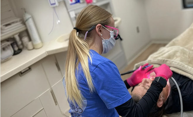 Female dental hygienist named Madison treating a male patient wearing protective glasses and a dental bib in a clinical setting