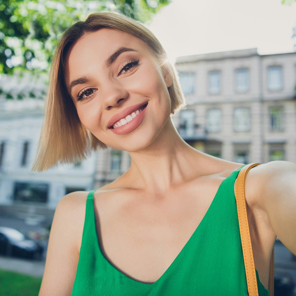 Young woman taking a smiling selfie in a park