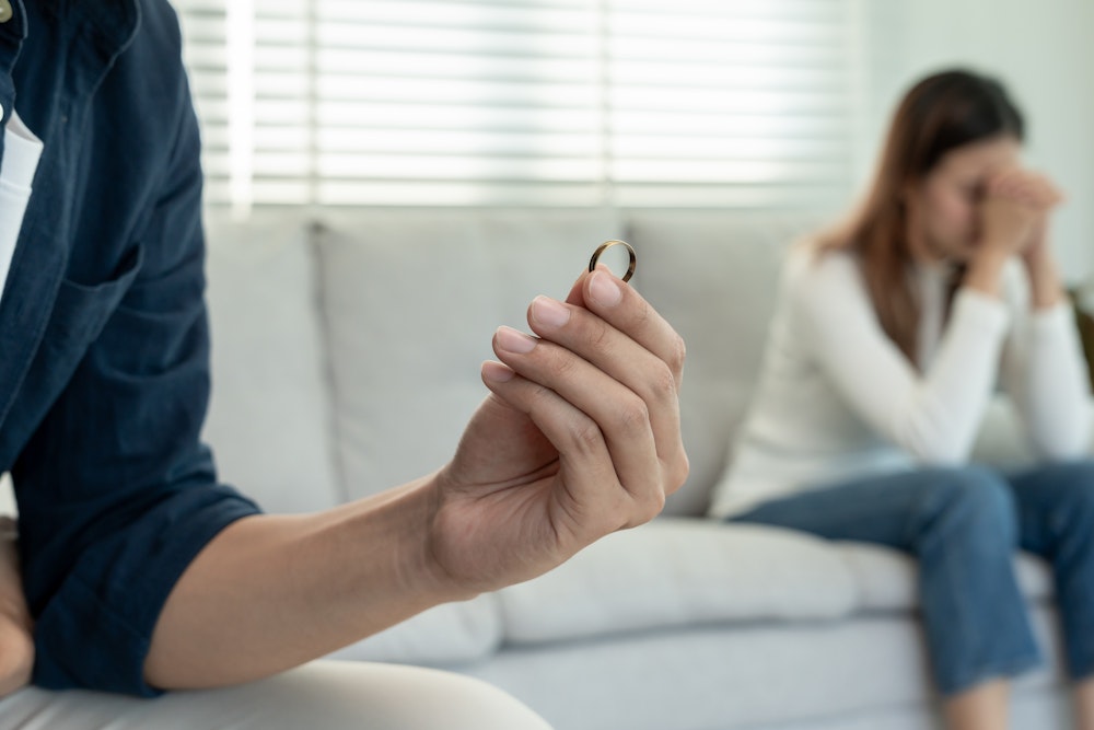 Man holding wedding ring with sad woman in the background