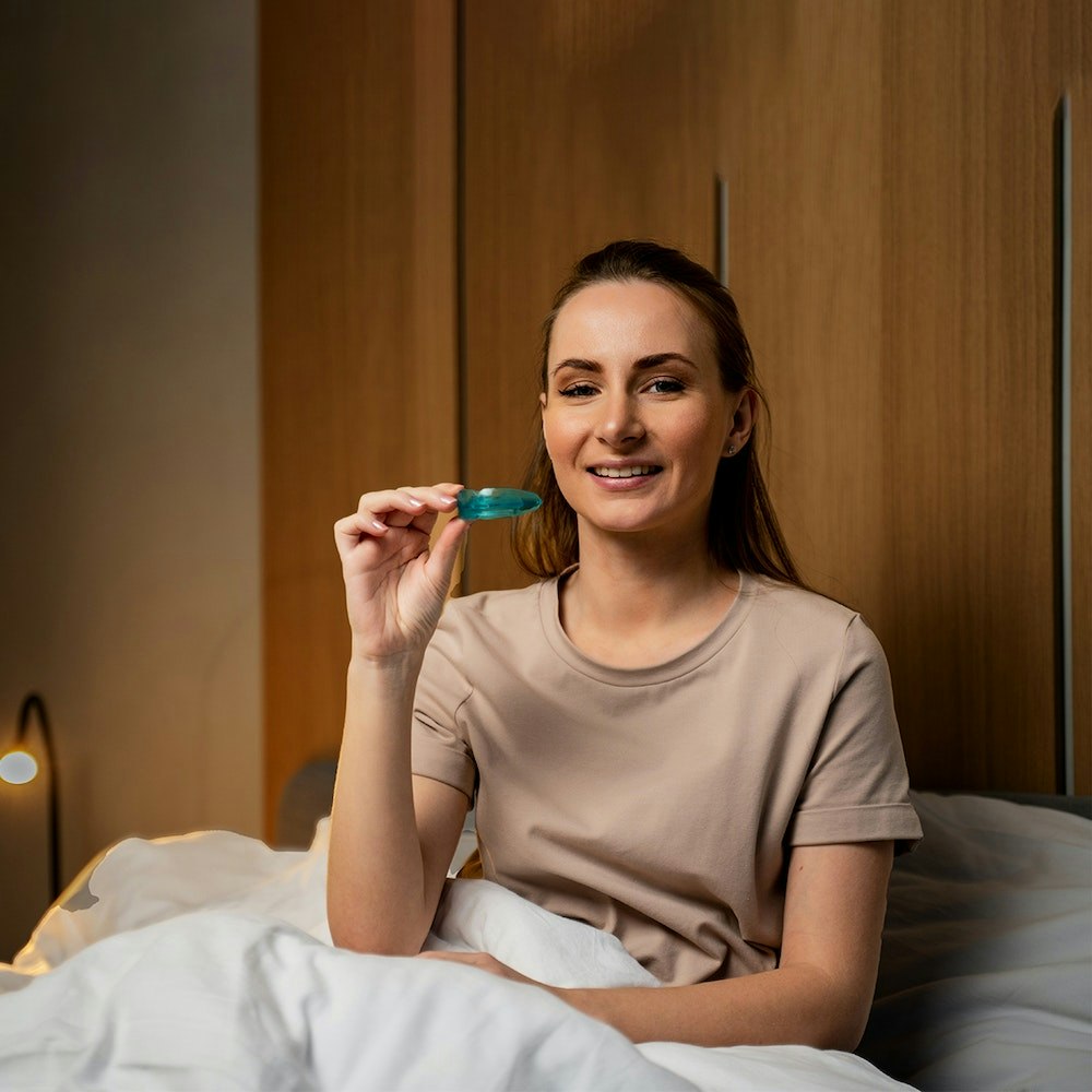 Young woman in bed holding up her night guard