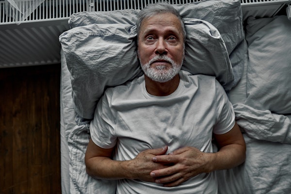 Older man lying awake in bed at night