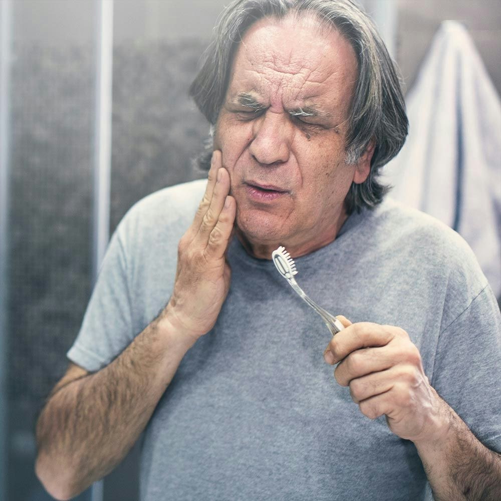 Older man holding jaw in pain after brushing teeth