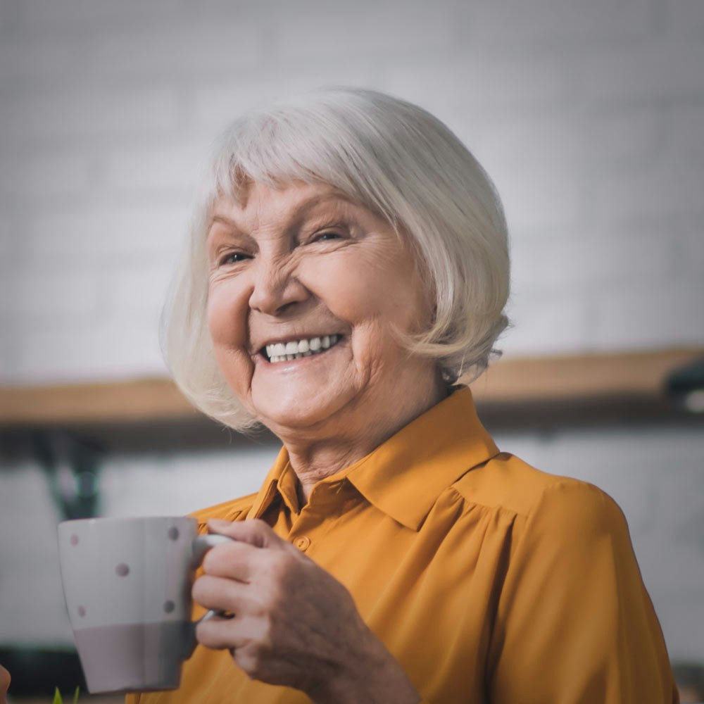 Smiling elderly woman with dental implants drinking coffee with grandson